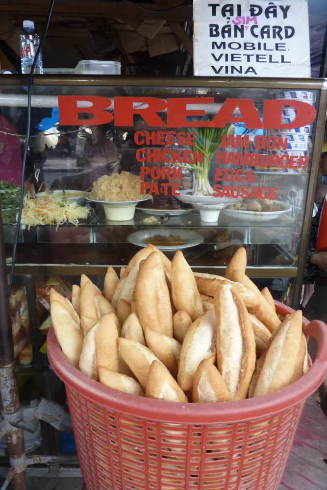 Basket of unfilled Vietnamese baguette rolls in front of a sandwich stall